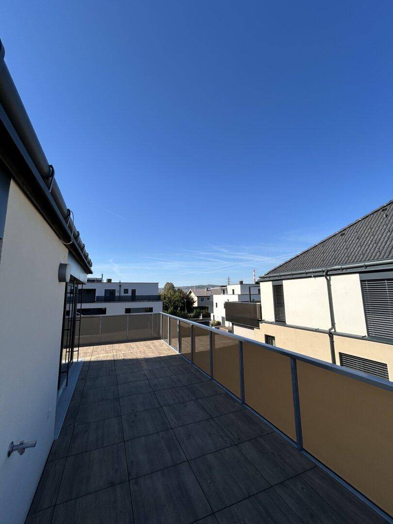 Großer Balkon mit Fliesenboden und Glasgeländer, umgeben von modernen Wohngebäuden.