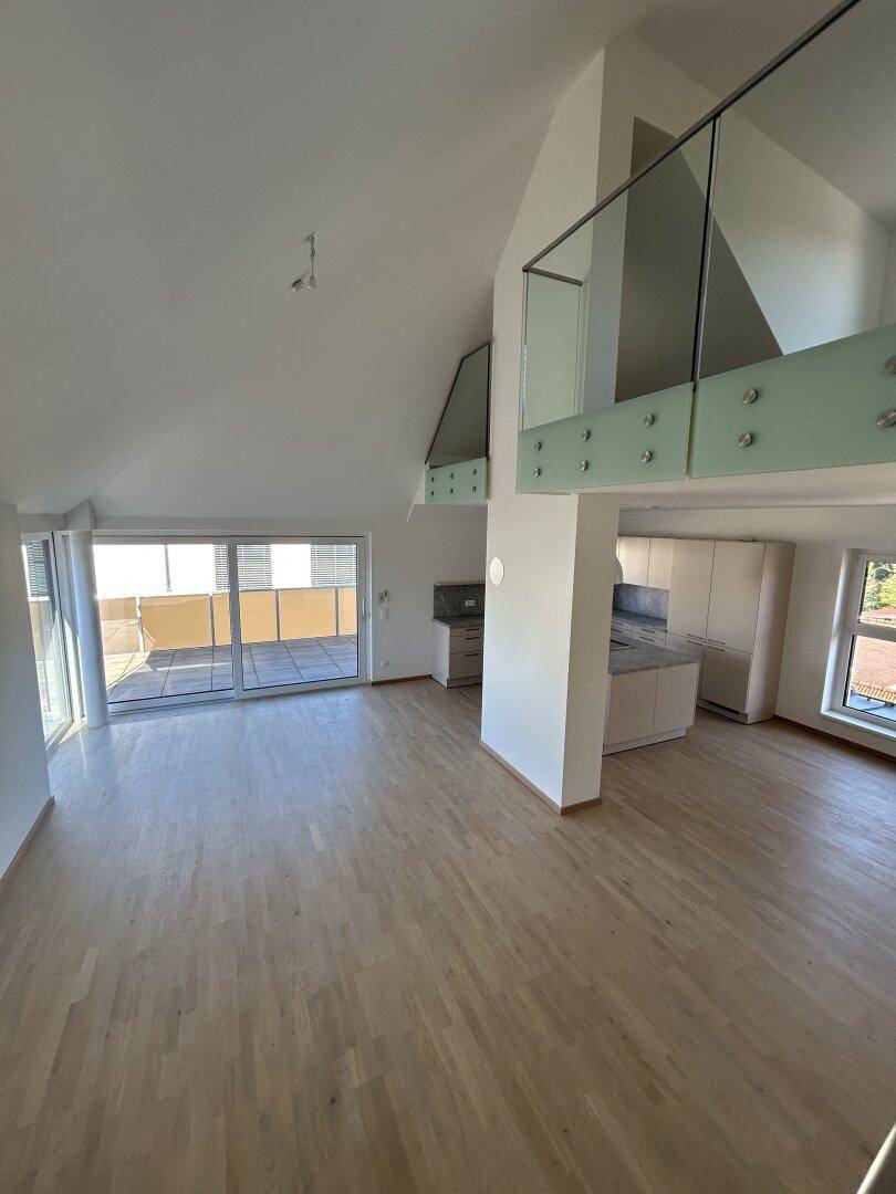 Heller offener Wohnbereich mit Dachschrägen, Holzparkett und Zugang zur Terrasse.
