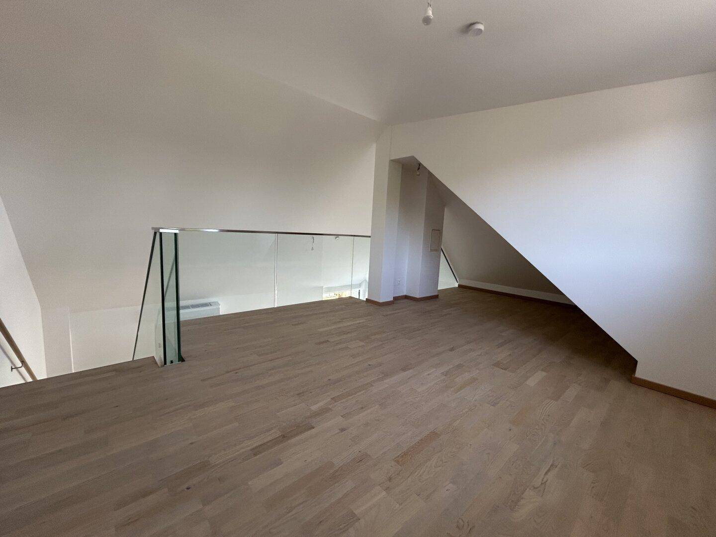 Heller Galeriebereich im Obergeschoss mit Parkettboden, Glasgeländer und Dachschrägen.