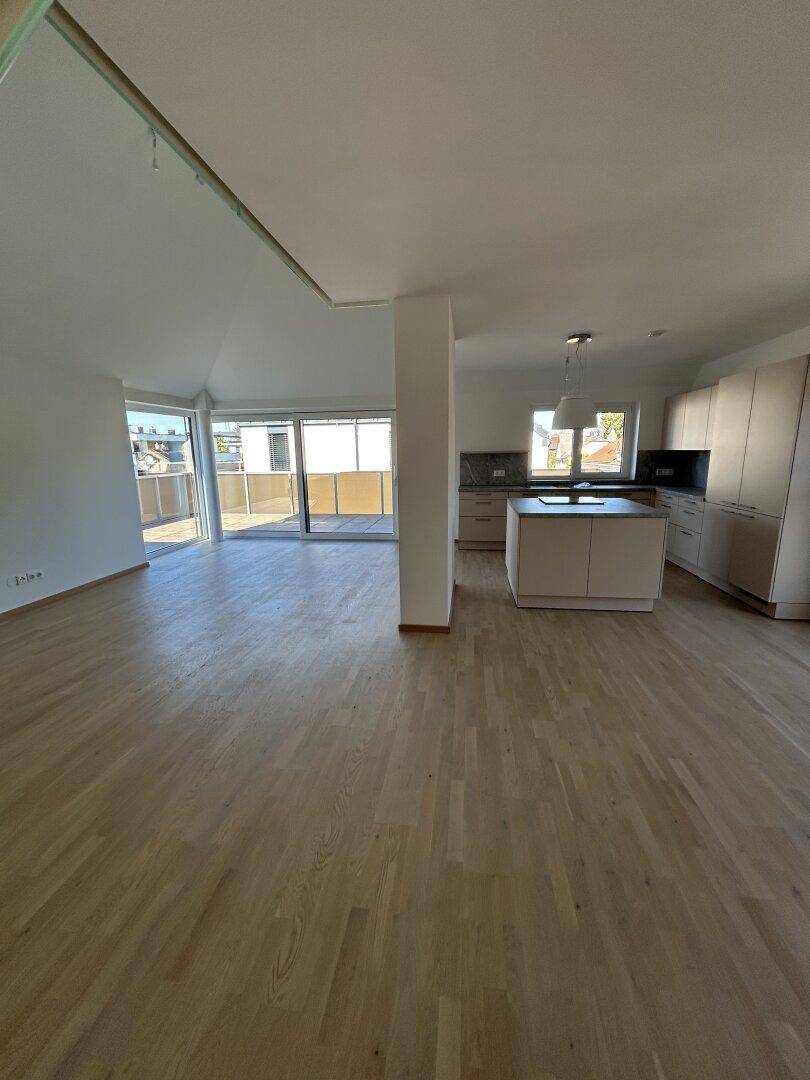 Heller offener Wohnbereich mit moderner Einbauküche, Holzparkett und Terrassenzugang.