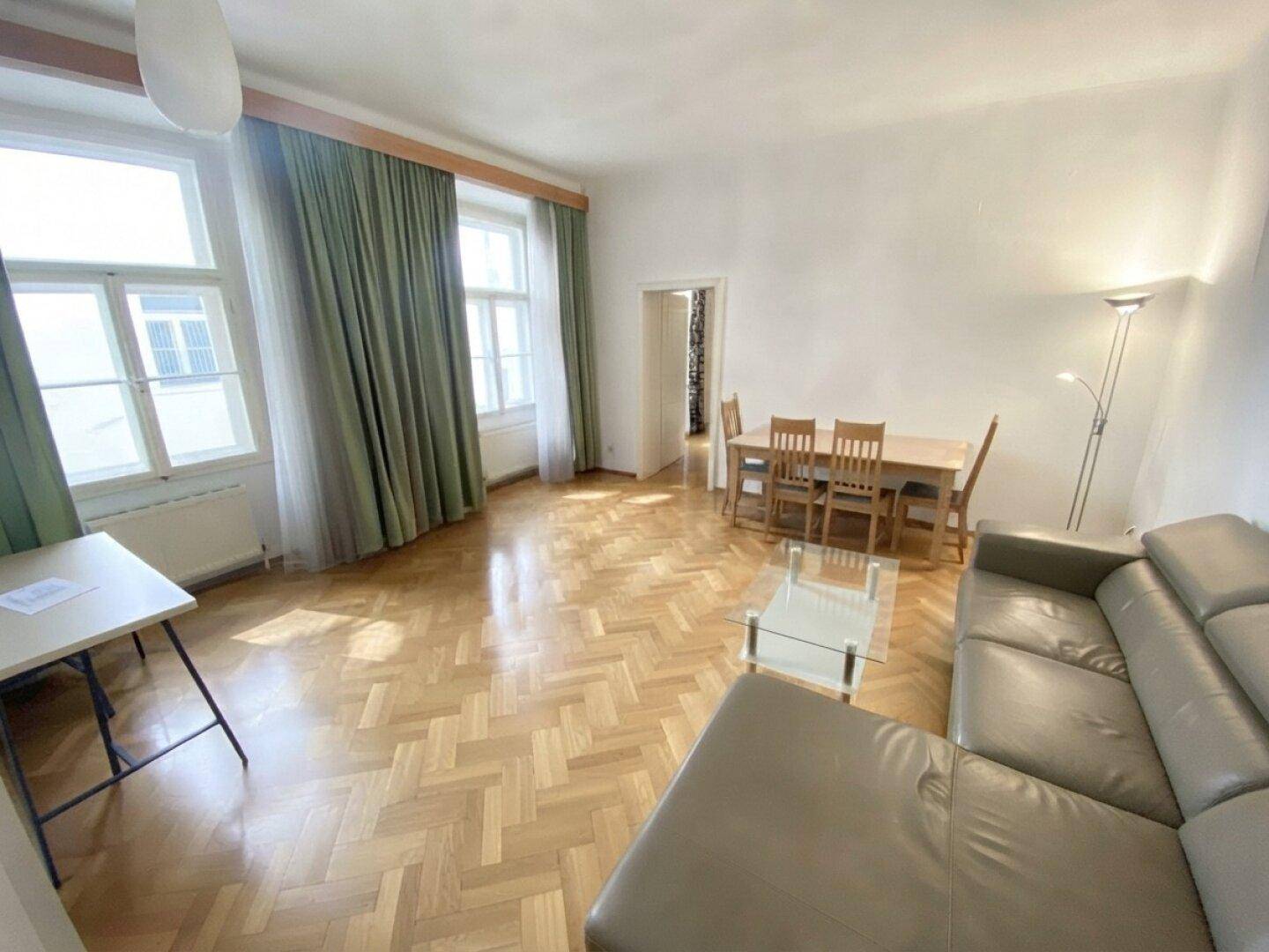 Heller Wohn-Essbereich mit großen Fenstern, die viel Tageslicht hereinlassen, und klassischem Parkettboden.