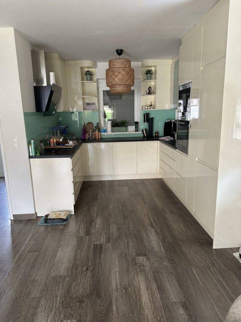 Moderne Küche mit cremefarbenen Hochglanzfronten, dunkler Arbeitsplatte und Holzoptikboden.