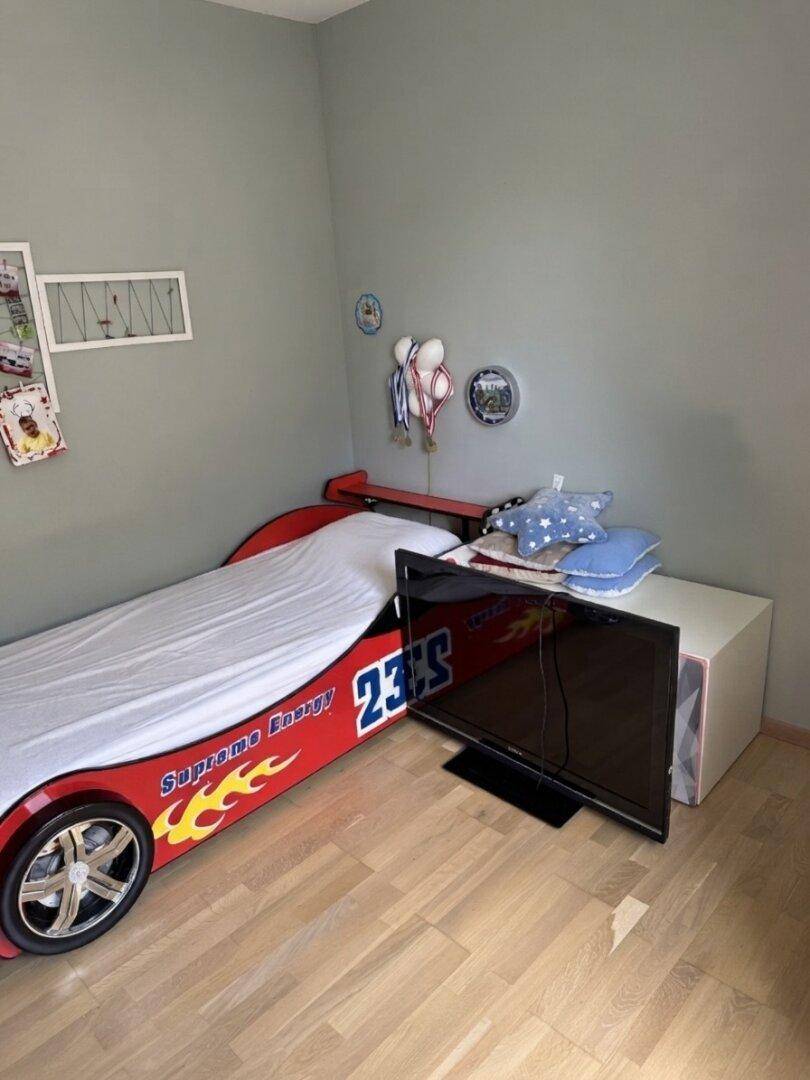 Detailansicht des Kinderzimmers mit Rennauto-Bett, Fernseher und hellem Holzfußboden.