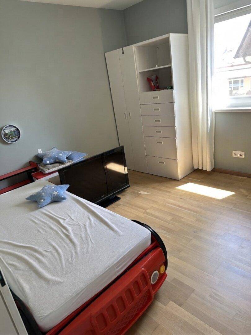 Kinderzimmer mit einem roten Rennauto-Bett, hellem Laminatboden und einem weißen Kleiderschrank.