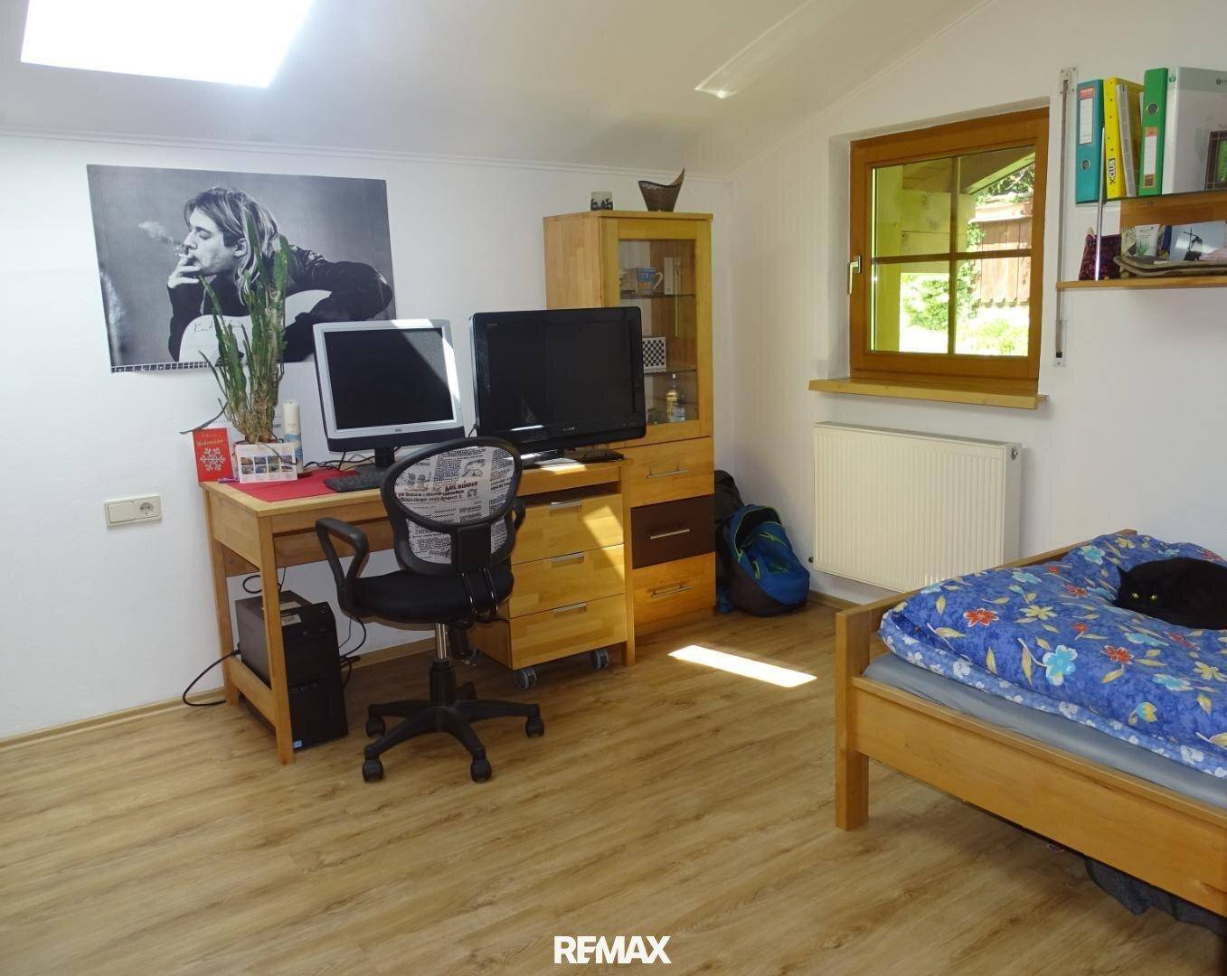 Helles Schlafzimmer mit Holzboden, Schreibtisch und Fenster mit Blick ins Grüne.