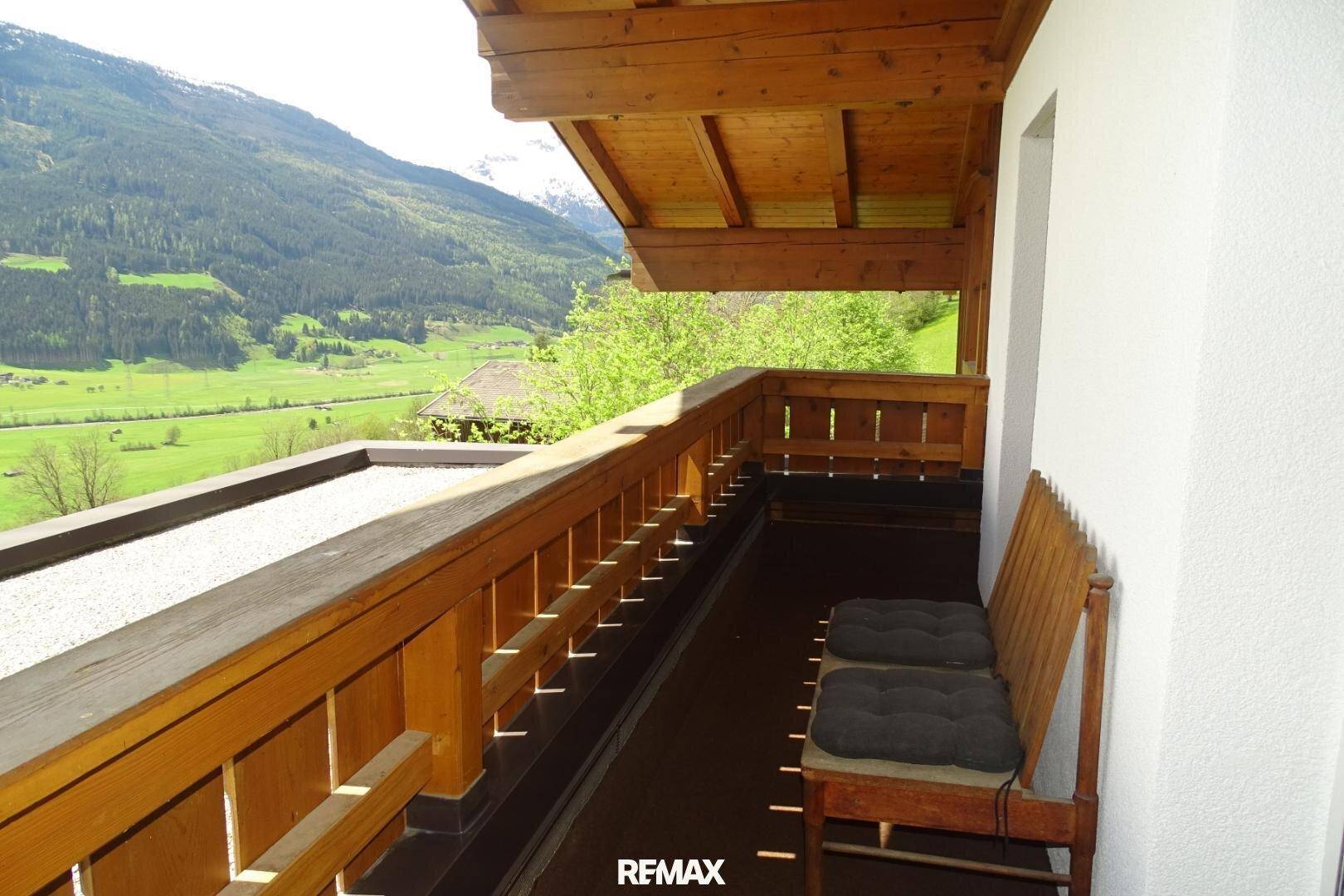 Traditioneller Holzbalkon mit Sitzgelegenheiten und weitem Blick auf die umliegende Berglandschaft.