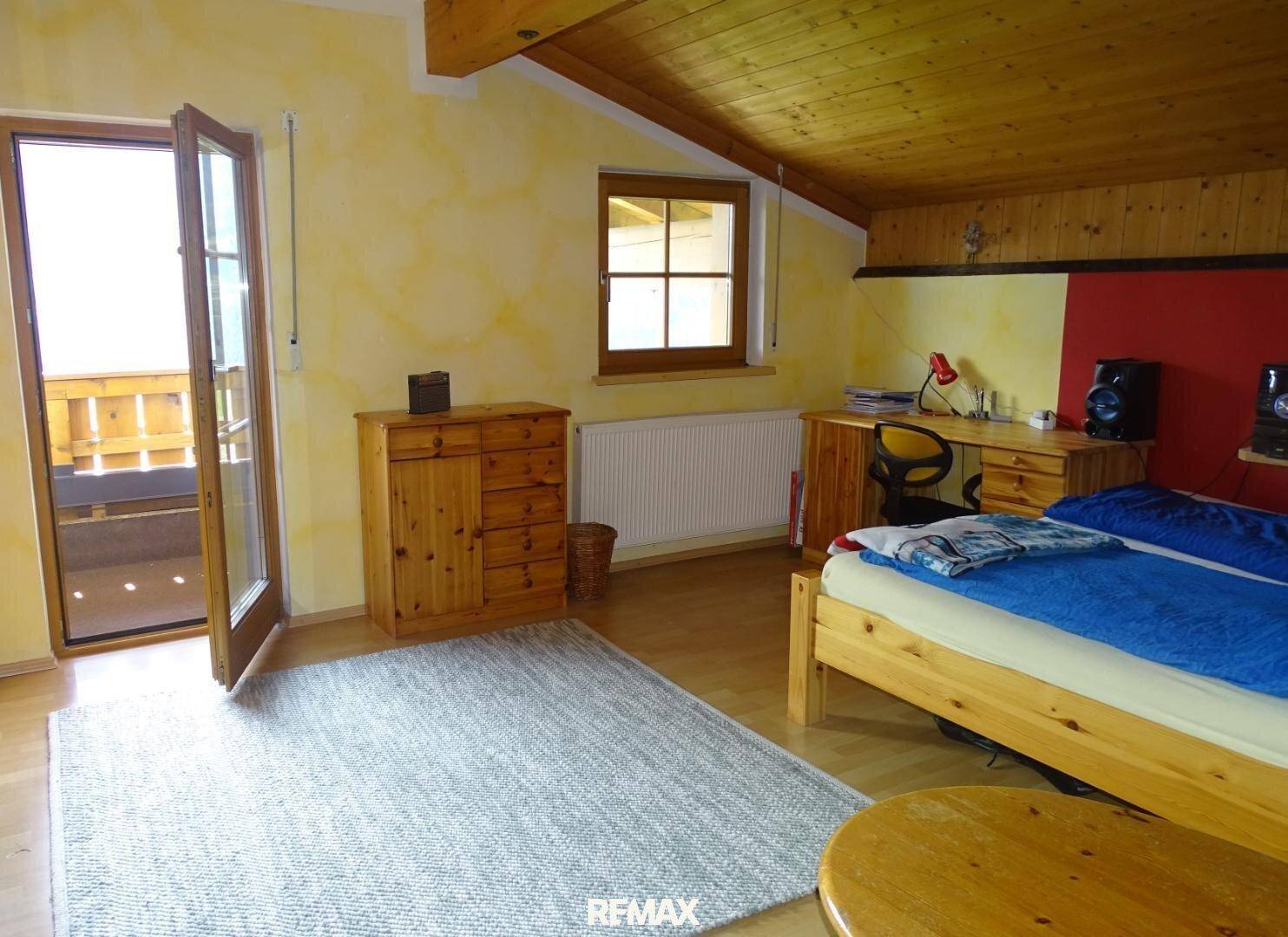 Rustikales Schlafzimmer mit Holzbalkendecke, Holzboden und Zugang zu einem Balkon.