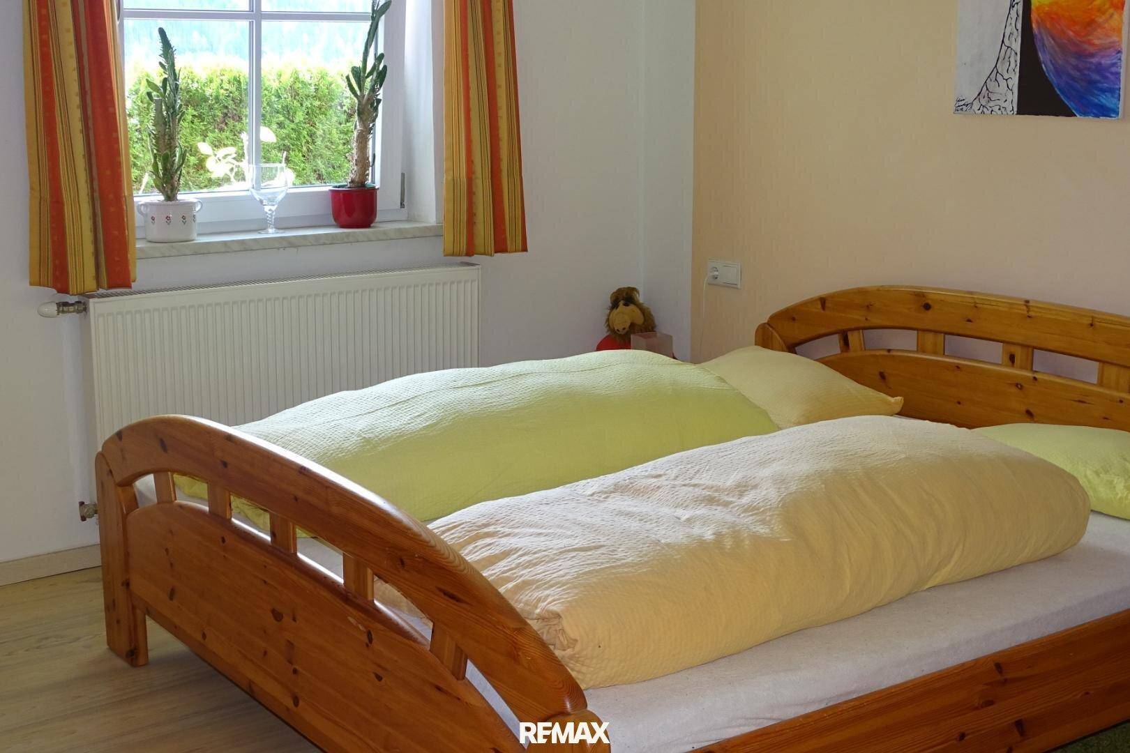 Helles Schlafzimmer mit zwei Einzelbetten aus Holz und einem Fenster mit Blick auf die Hecke.