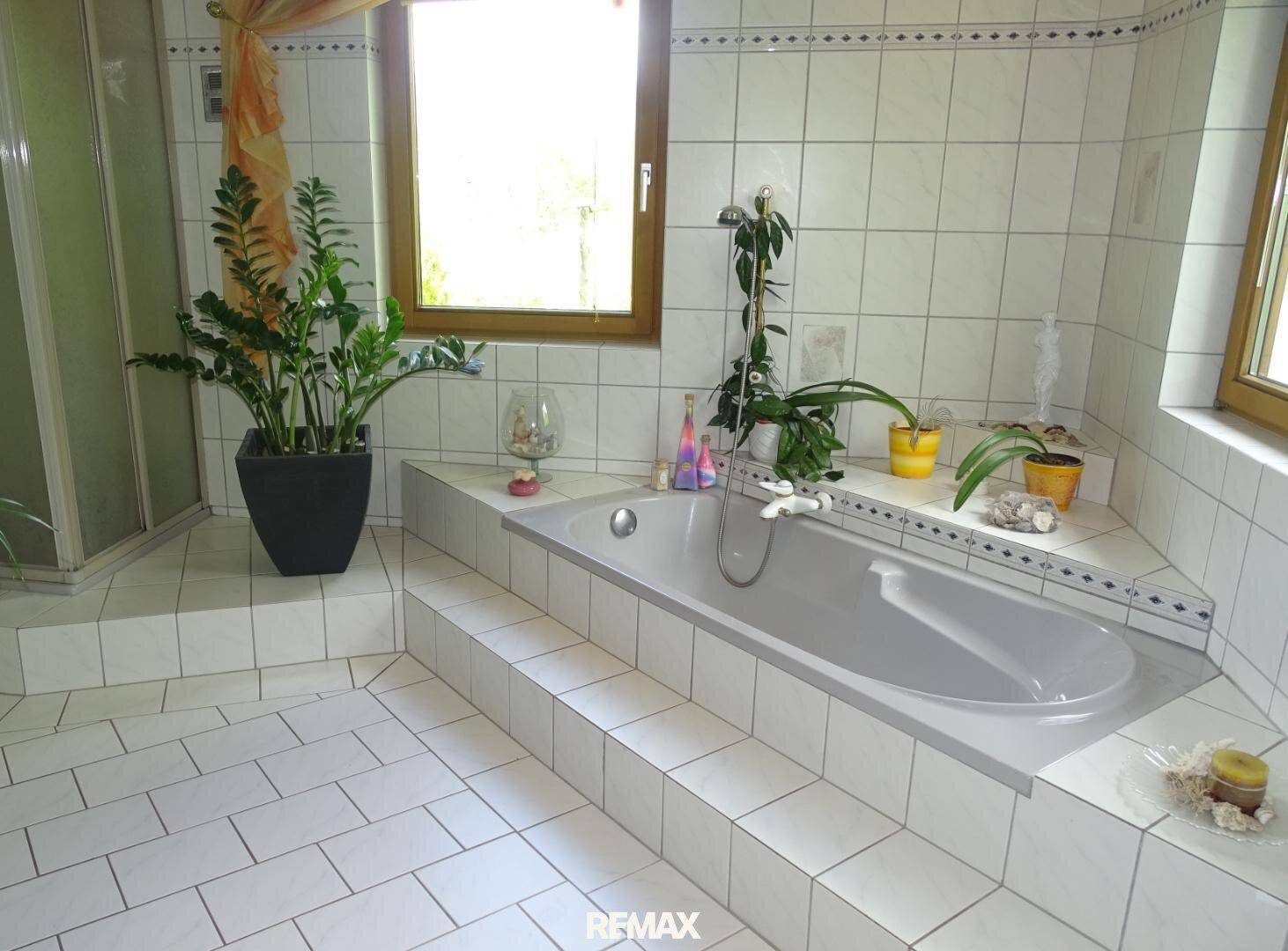 Geräumiges Badezimmer mit weiß gefliesten Wänden und einer eingelassenen Badewanne am Fenster.