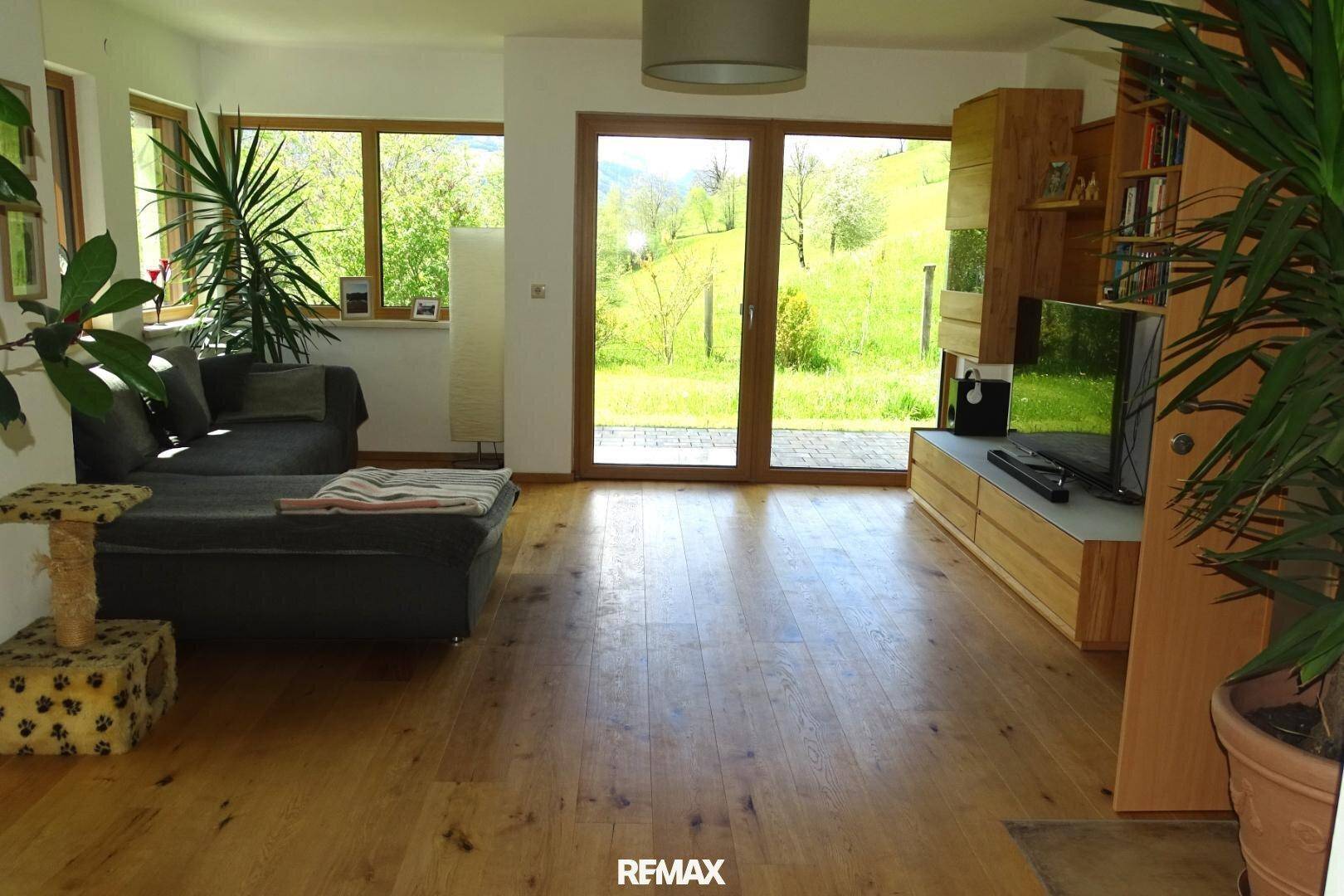 Helles Wohnzimmer mit Holzboden und Zugang zur Terrasse, umgeben von grüner Natur.