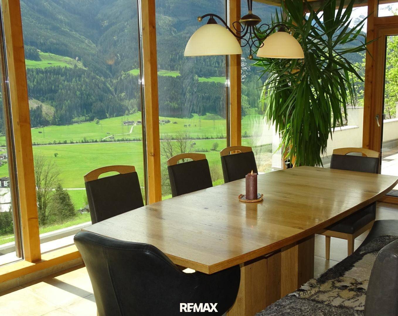 Heller Essbereich mit großem Holztisch und raumhohen Fenstern, die einen weiten Blick ins Grüne bieten.