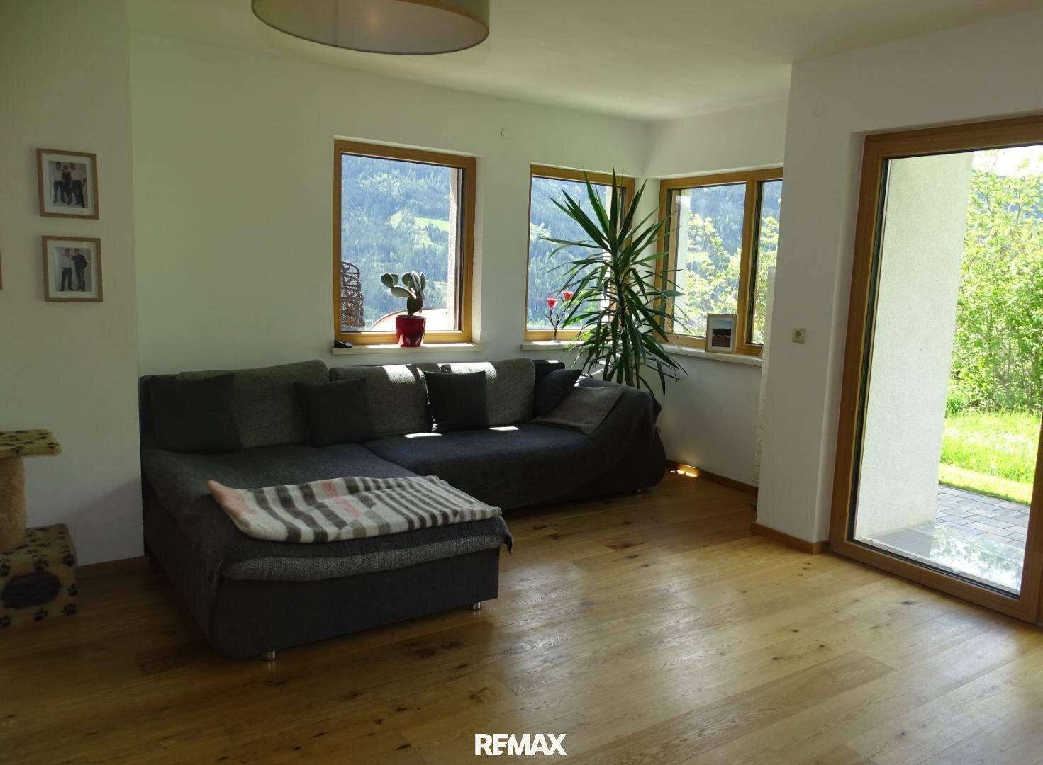 Gemütliches Wohnzimmer mit bequemer Couch, Holzboden und großen Fenstern mit Bergblick.