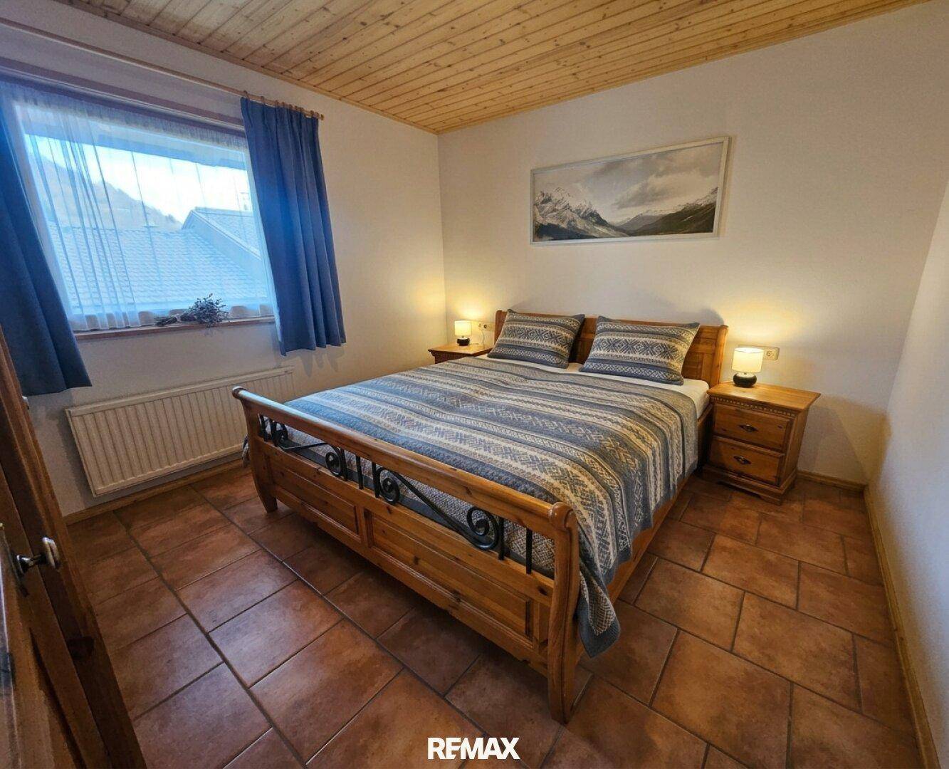 Rustikales Schlafzimmer mit Holzdoppelbett, Terrakottaboden und Blick ins Grüne.