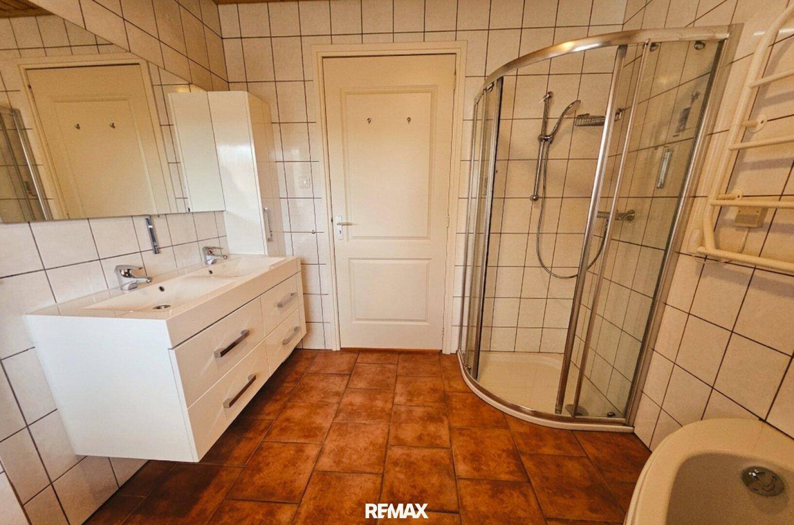 Badezimmer mit Doppelwaschbecken, Duschkabine und Terrakottafliesen.