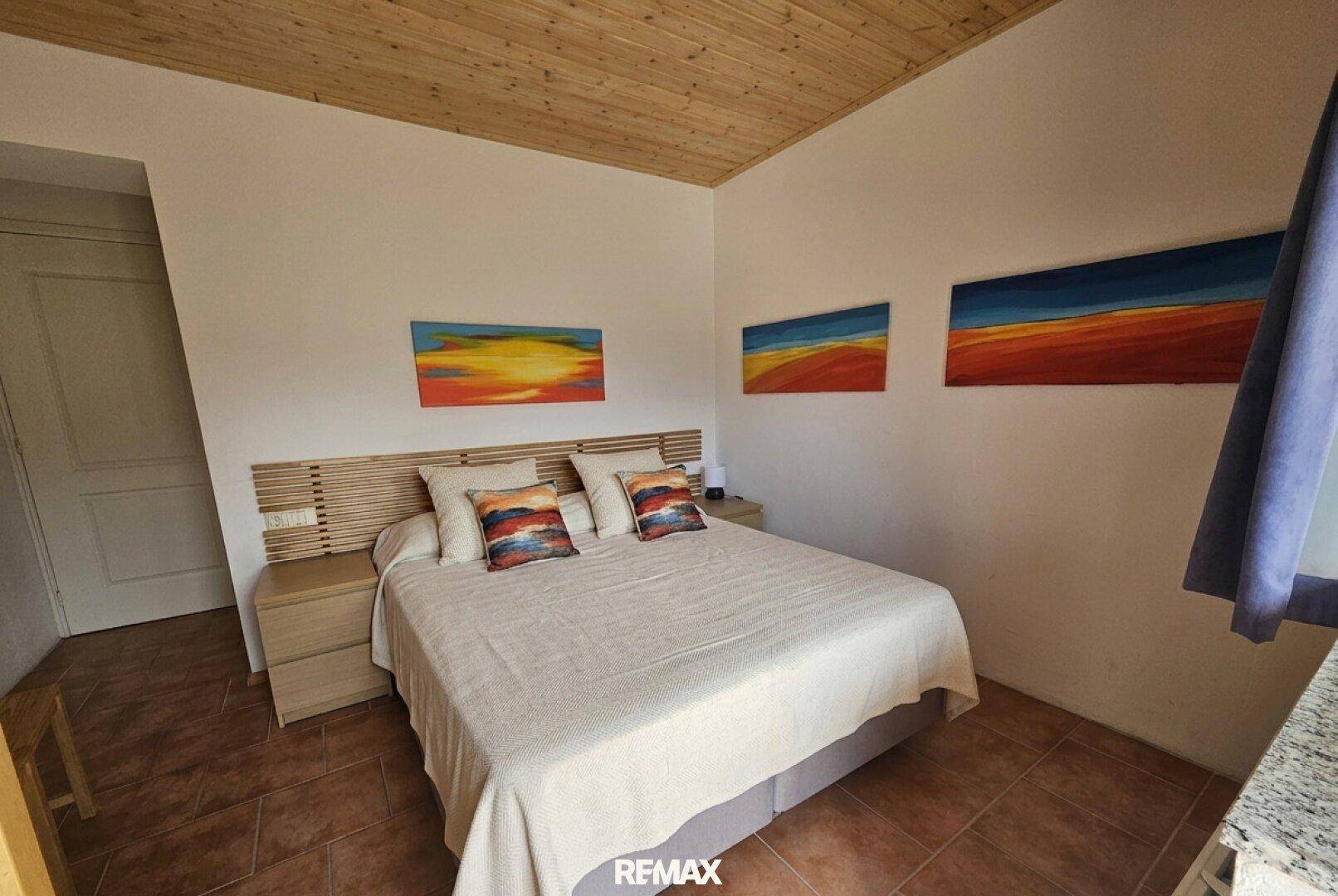 Schlafzimmer mit Doppelbett, Holzdecke und farbenfrohen Kunstwerken an der Wand.