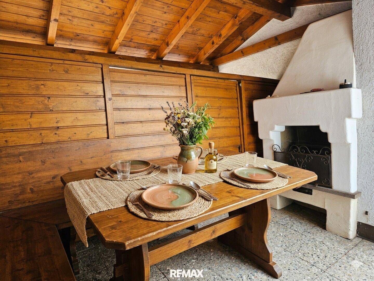 Überdachter Essbereich im Freien mit Holztisch, Bänken und integriertem Grillkamin.