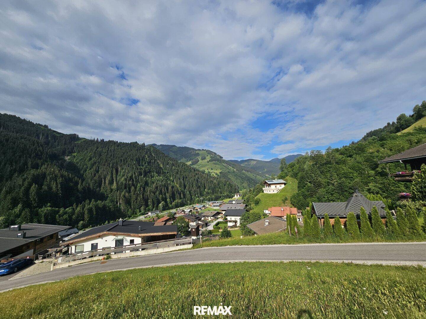Weitblick über ein malerisches Dorf im Tal, umgeben von bewaldeten Berghängen unter blauem Himmel.