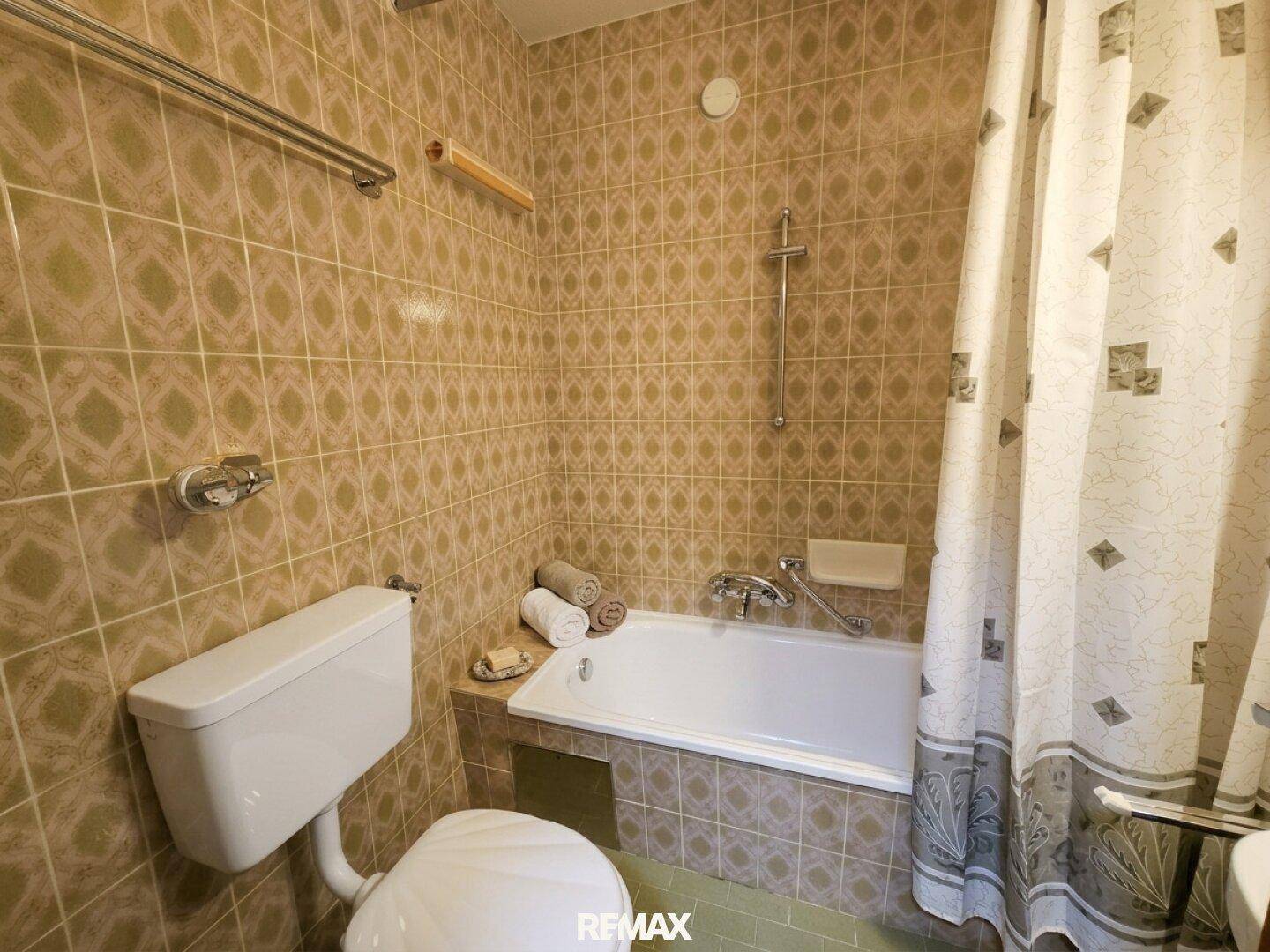 Badezimmer mit Badewanne, Duschvorhang und gemusterten Fliesen im 80er-Jahre-Stil.