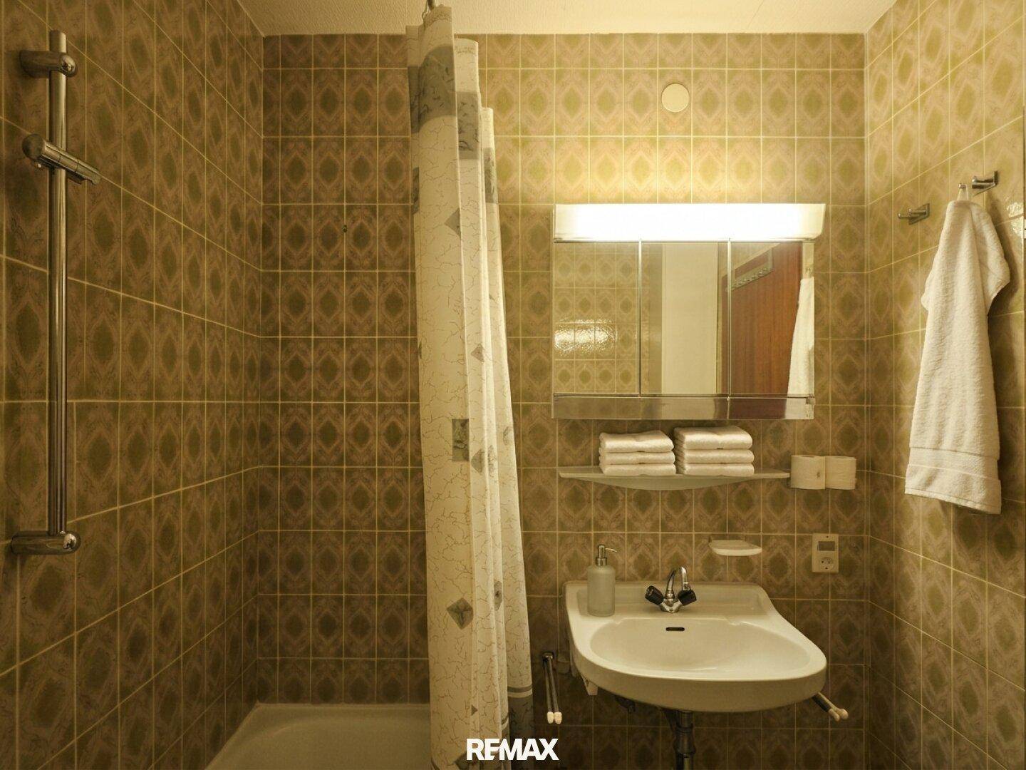 Badezimmer mit Waschbecken, Spiegelschrank und Duschbereich mit gemusterten Fliesen.