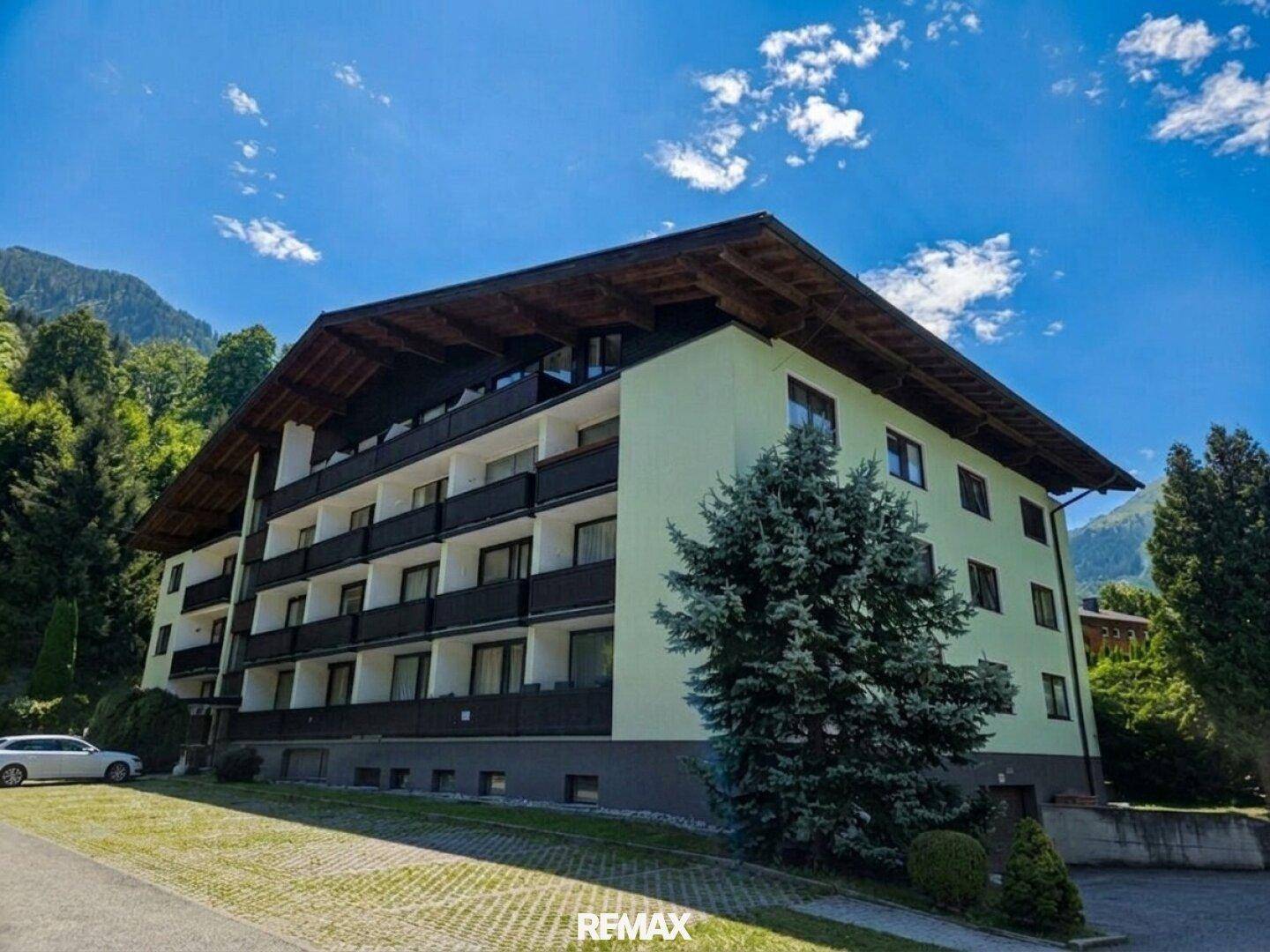 Mehrstöckiges Gebäude mit Balkonen, umgeben von grüner Berglandschaft.