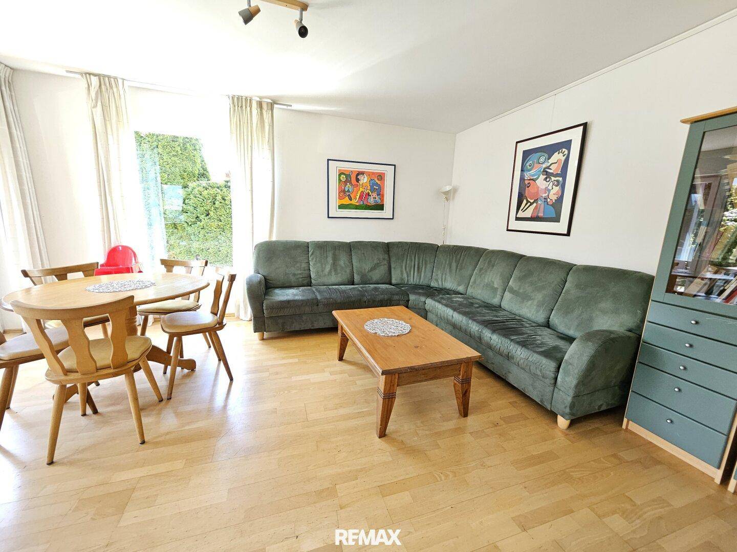 Gemütlicher Wohn-Essbereich mit grünem Ecksofa, Holztisch und hellem Parkettboden.