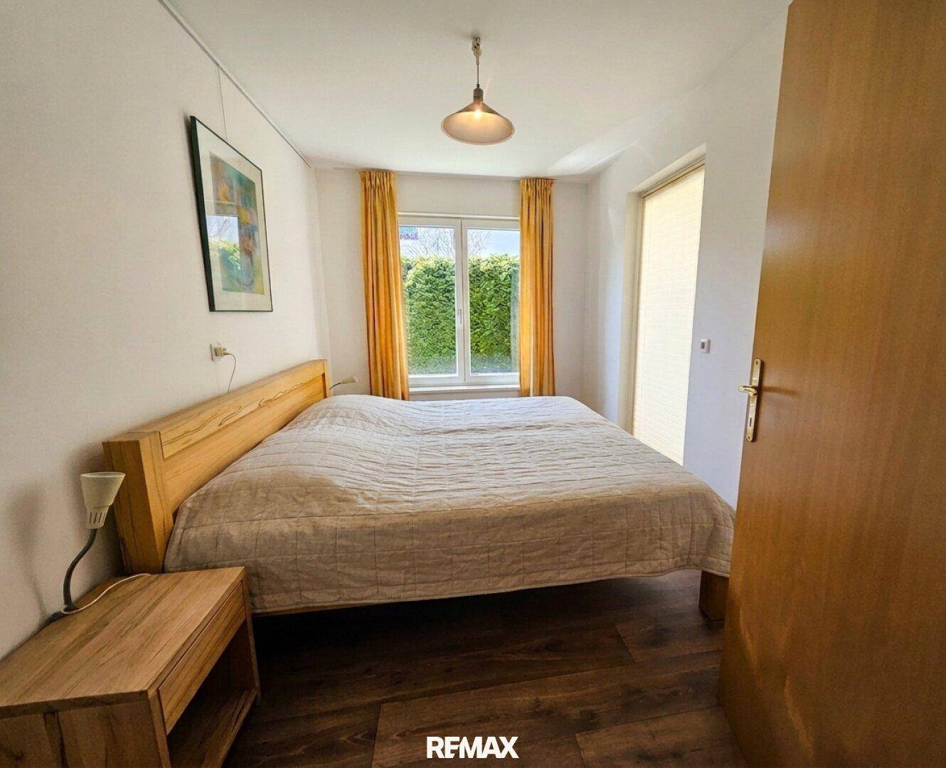 Schlafzimmer mit Doppelbett, Holznachttisch und Fenster mit Blick ins Grüne.