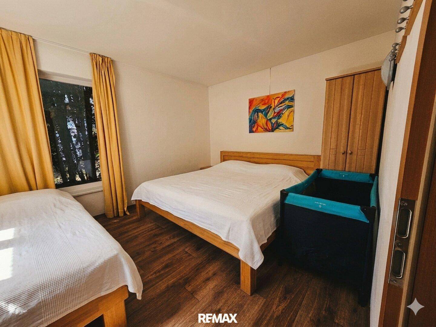 Schlafzimmer mit Doppelbett, Einzelbett, Babybett und Holzschrank.