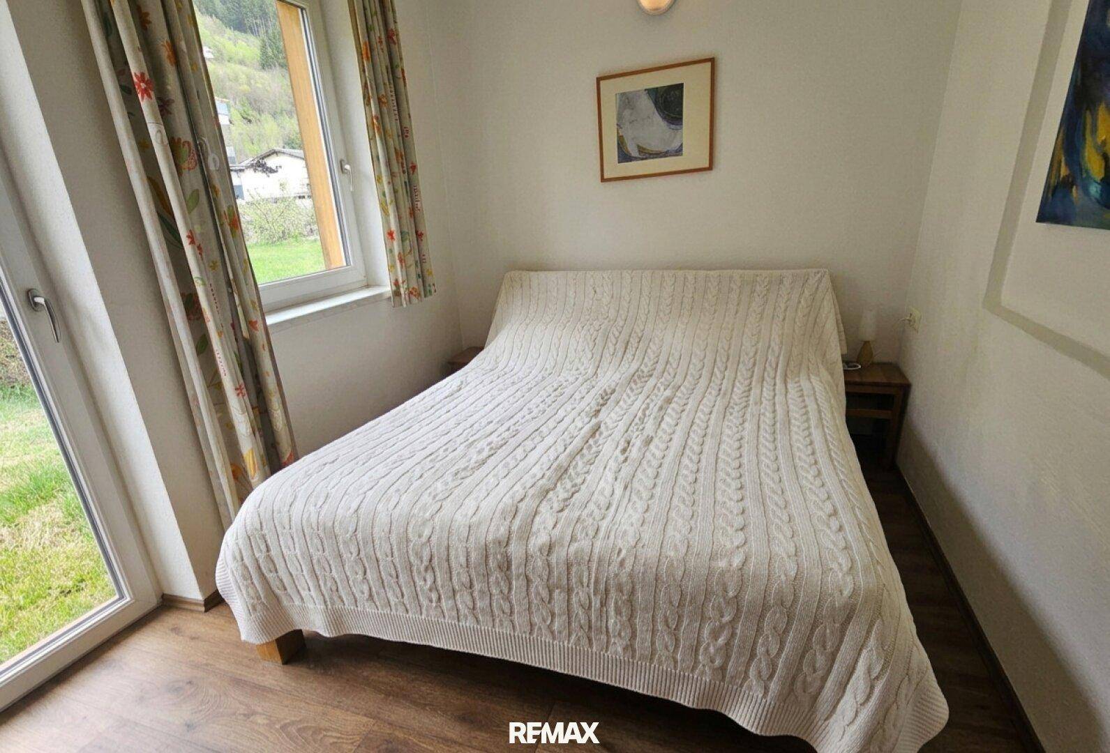 Schlafzimmer mit Doppelbett und großem Fenster mit Zugang zum Gartenbereich.