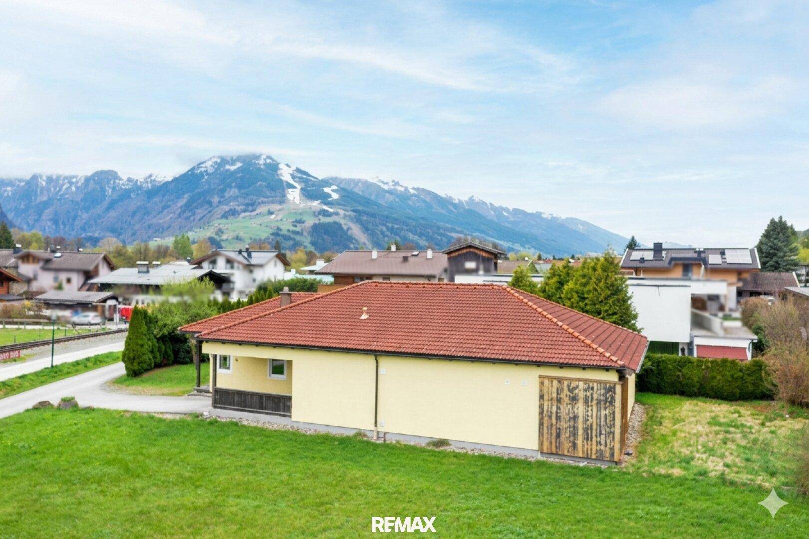 Seitenansicht des Hauses mit gelber Fassade, grünem Rasen und Bergblick im Hintergrund.