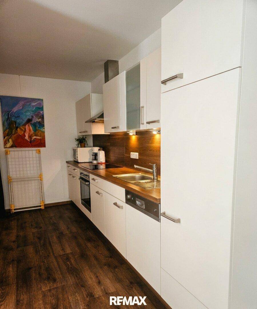 Moderne Küche mit weißen Schränken, Holzarbeitsplatten und dunklem Laminatboden.