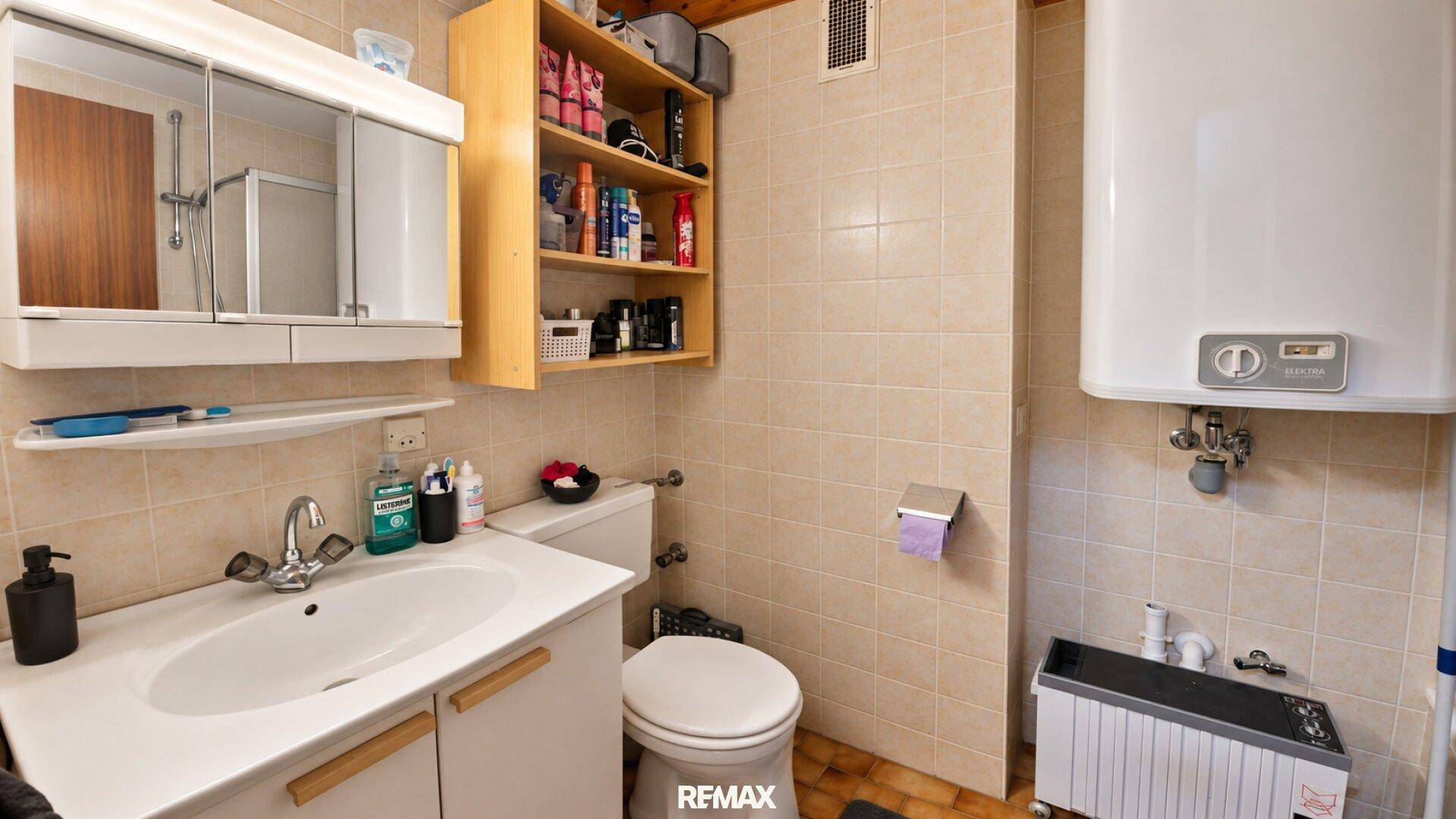 Funktionales Badezimmer mit beigefarbenen Fliesen, Waschbecken, Toilette und Spiegelschrank.