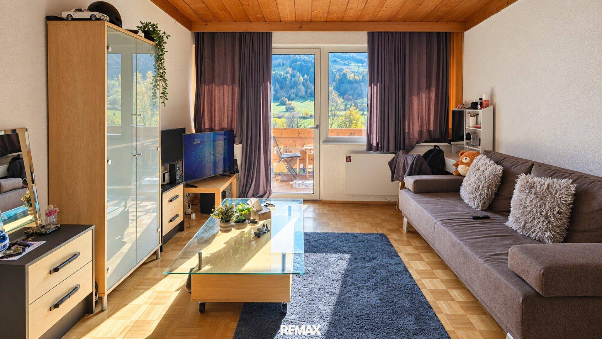 Helles Wohnzimmer mit Holzbalkendecke, Parkettboden und Zugang zu einem Balkon mit Bergblick.