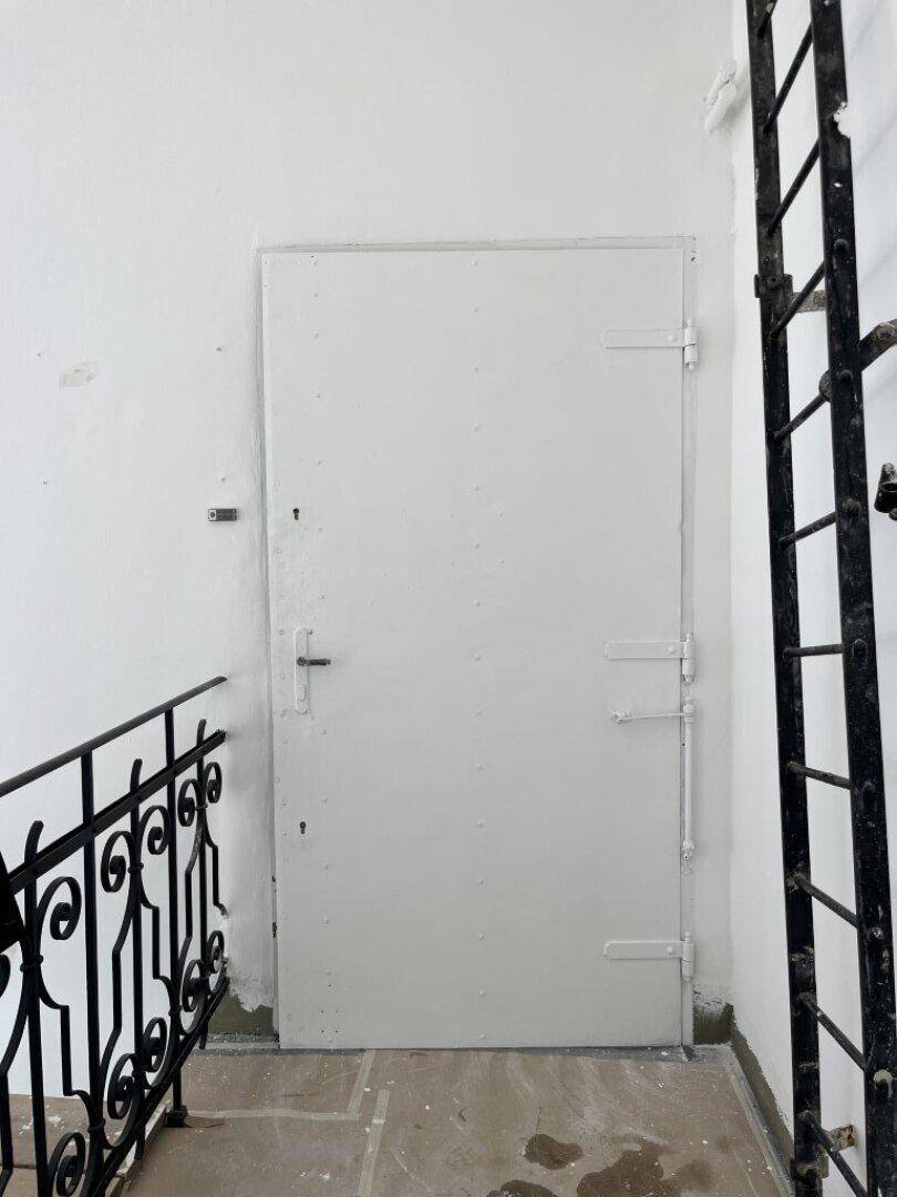 Flur mit einer schlichten weißen Tür und einem schmiedeeisernen Geländer, das zu einer Treppe führt.