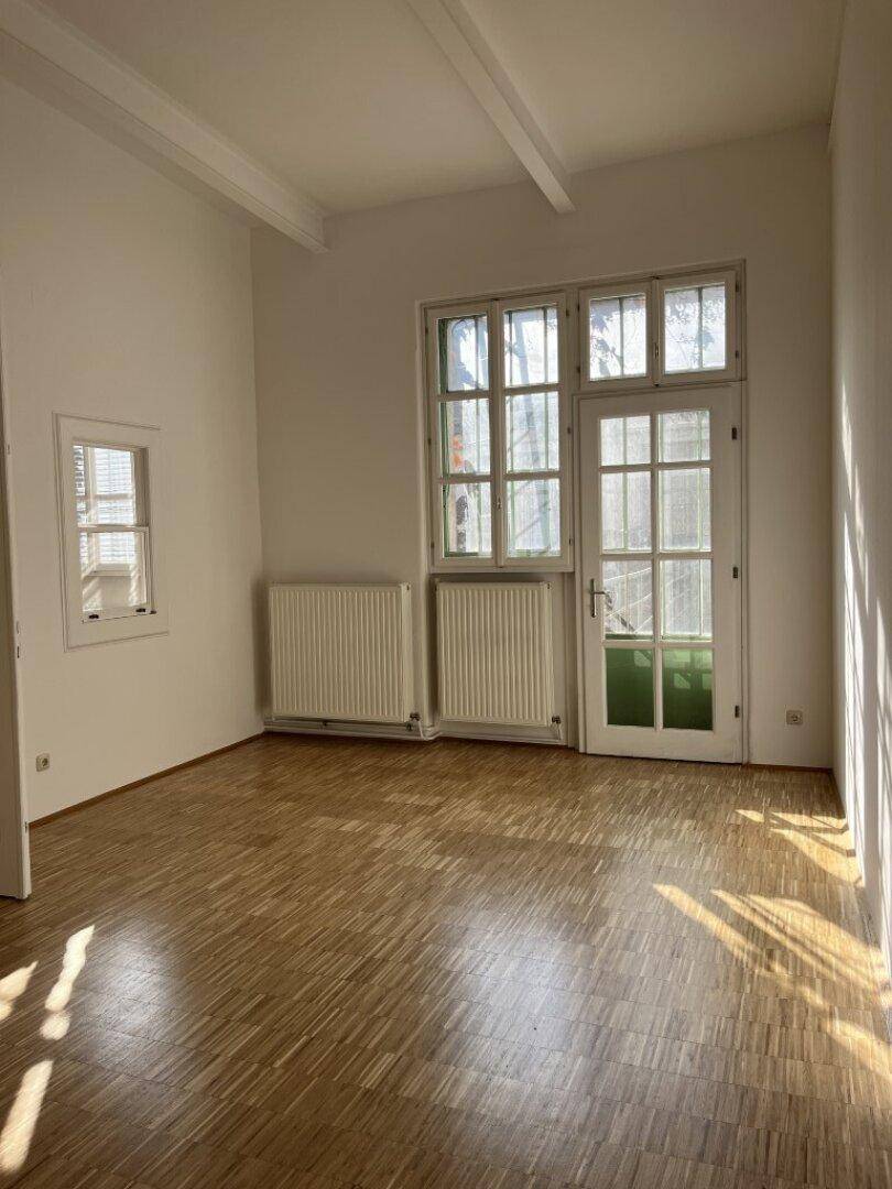 Heller Raum mit Holzboden, weißen Wänden und einer Tür mit Glaspaneelen, die viel Licht hereinlässt.