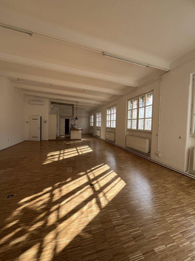 Geräumiger offener Wohnbereich mit Holzboden, hohen Decken und viel Sonnenlicht, das den Raum durchflutet.