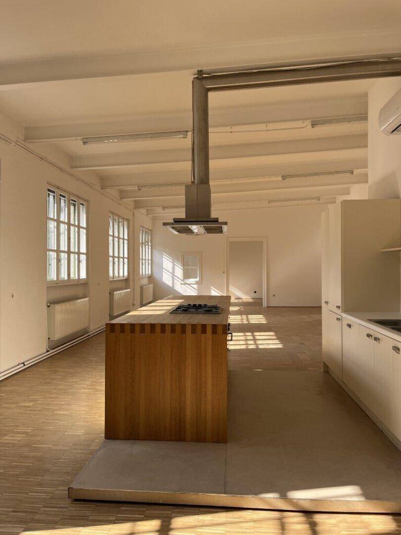 Offener Wohnbereich mit Kücheninsel, Holzarbeitsplatte und viel natürlichem Licht, das durch die Fenster fällt.
