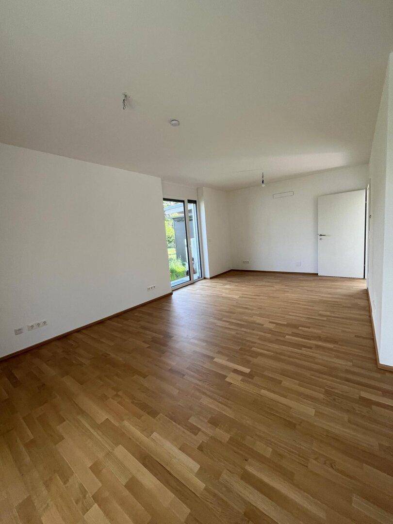 Geräumiges Wohnzimmer mit hellem Parkettboden und Zugang zu einem Außenbereich.