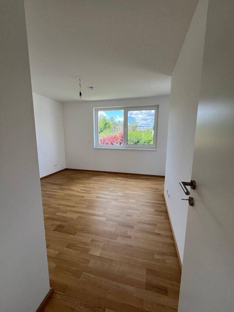 Helles Schlafzimmer mit Parkettboden und großem Fenster, das viel Licht spendet.