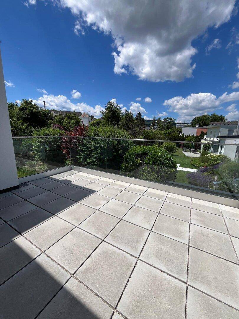 Geräumiger Balkon mit Fliesenboden und Glasgeländer, bietet Blick ins Grüne.