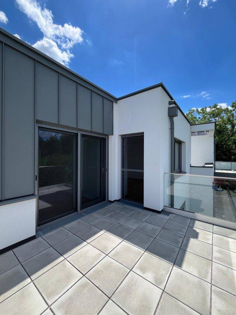 Große Dachterrasse mit Fliesenboden und Glasgeländer, bietet weite Ausblicke.
