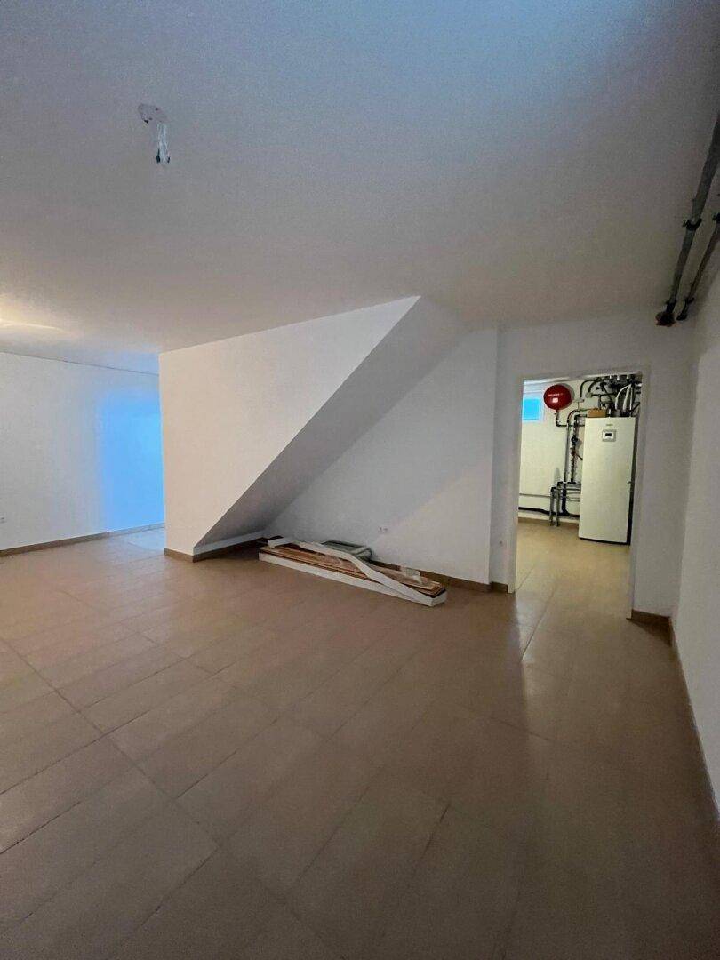 Kellerbereich mit Fliesenboden und Zugang zu einem Technikraum mit Heizungsanlage.