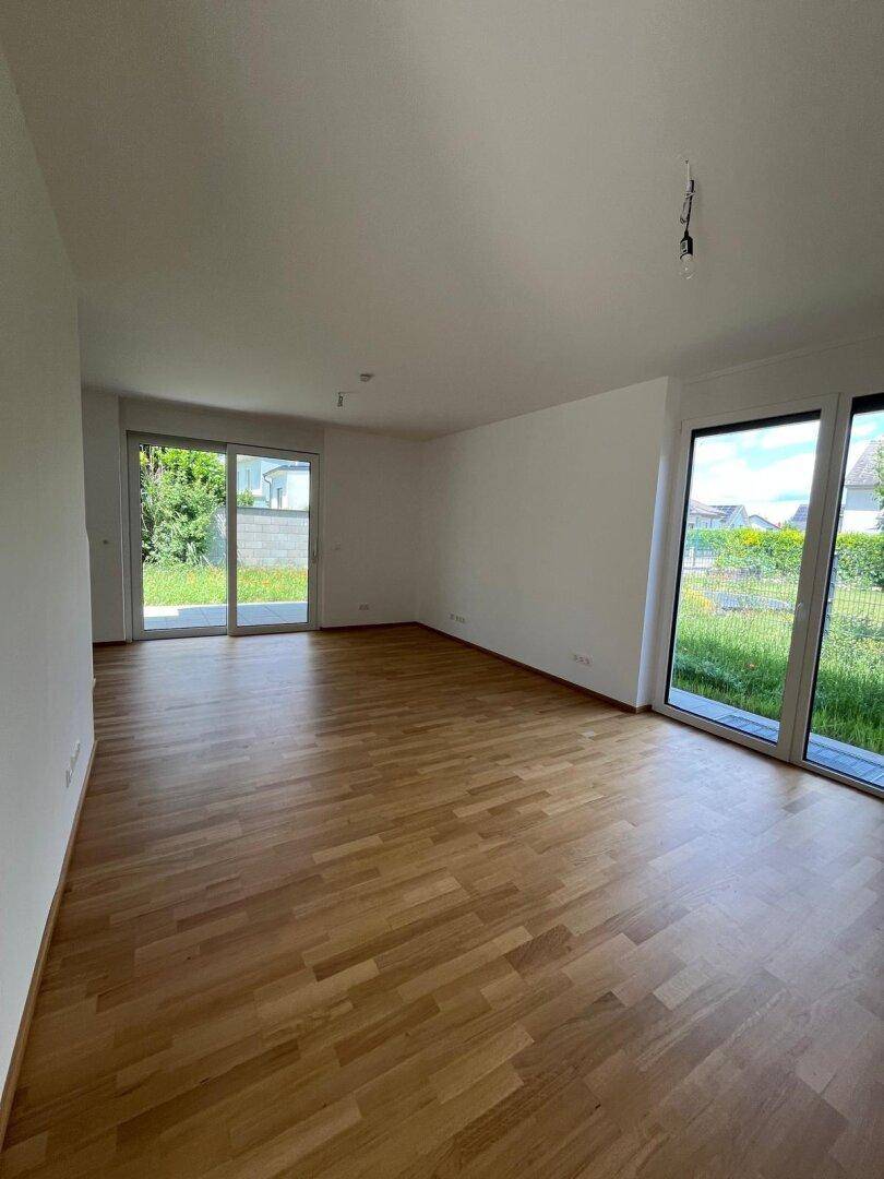 Geräumiges Wohnzimmer mit hellem Parkettboden und großen Fenstern mit Blick ins Grüne.