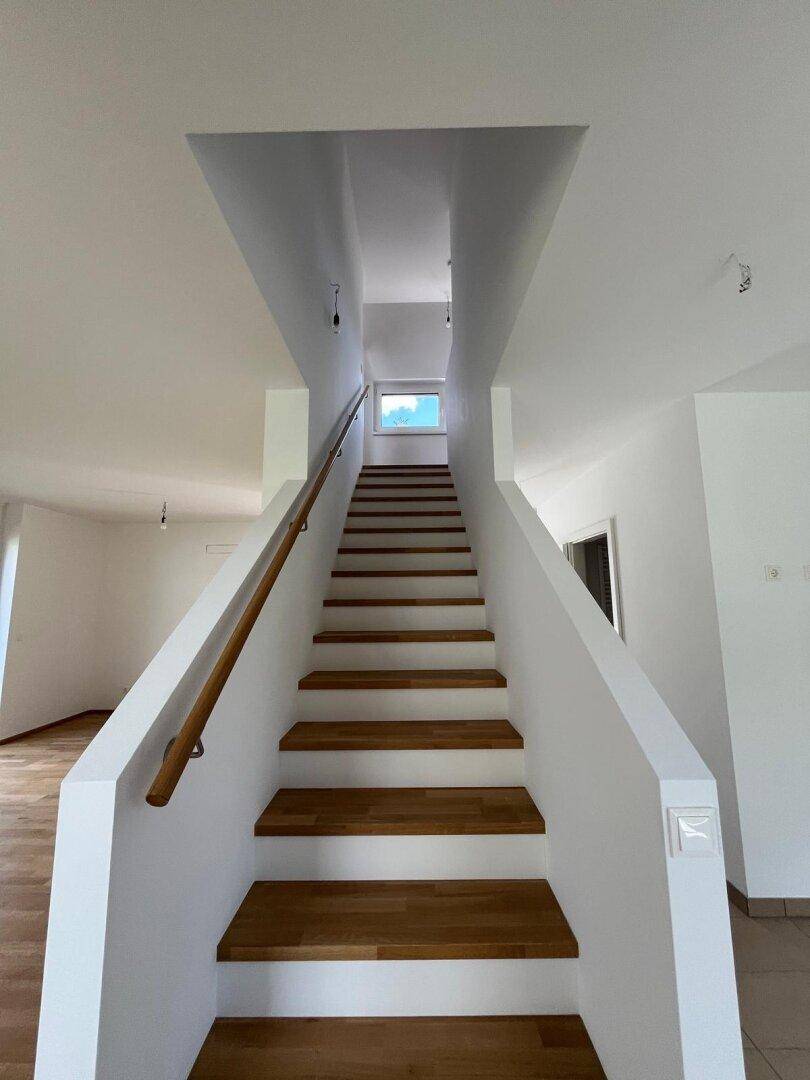 Modernes Treppenhaus mit Holzstufen und weißem Geländer, das in die oberen Etagen führt.