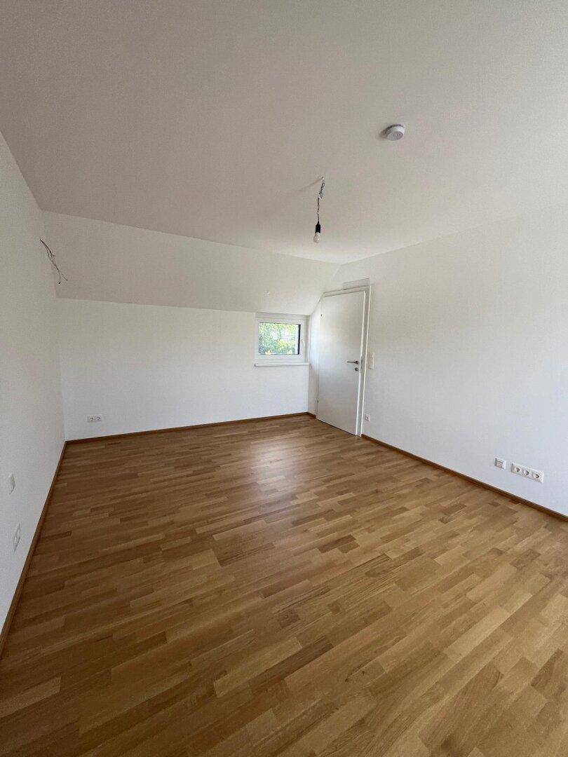 Helles Schlafzimmer im Dachgeschoss mit Parkettboden, Dachschräge und Fenster.