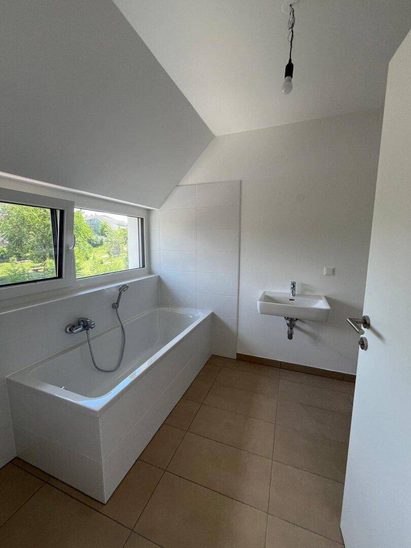 Modernes Badezimmer mit Badewanne, Waschbecken und Fenster unter einer Dachschräge.