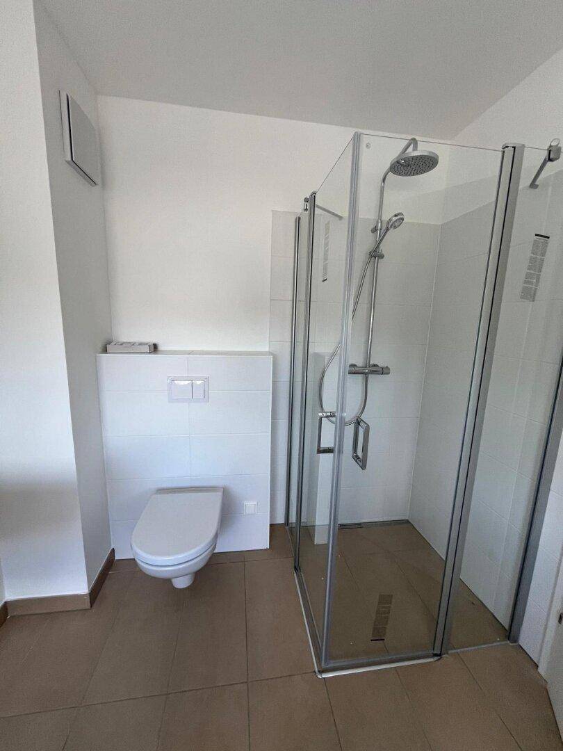 Modernes Badezimmer mit ebenerdiger Dusche und wandhängendem WC, hell gefliest.