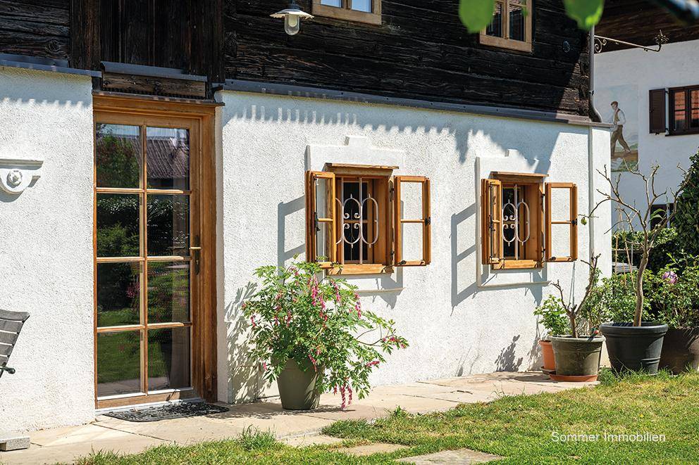 Detailansicht der weißen Hausfassade mit Holztür, kleinen Fenstern und dekorativen Pflanzen im Vorgarten.