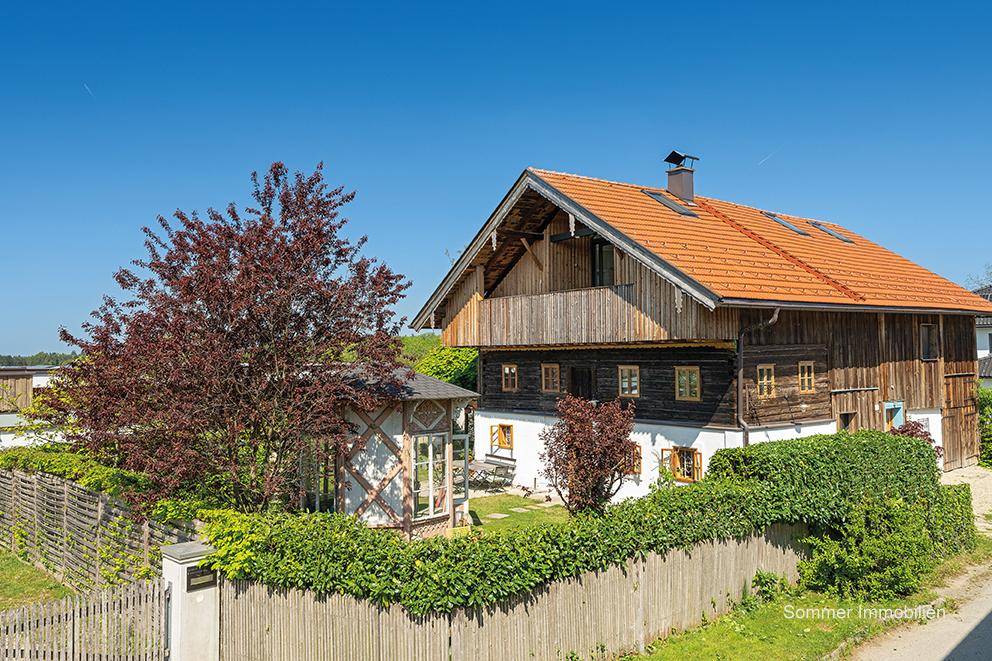 Charmantes Landhaus mit Holzbalkonen, rotem Ziegeldach und einem gepflegten Garten mit Hecke und Bäumen.