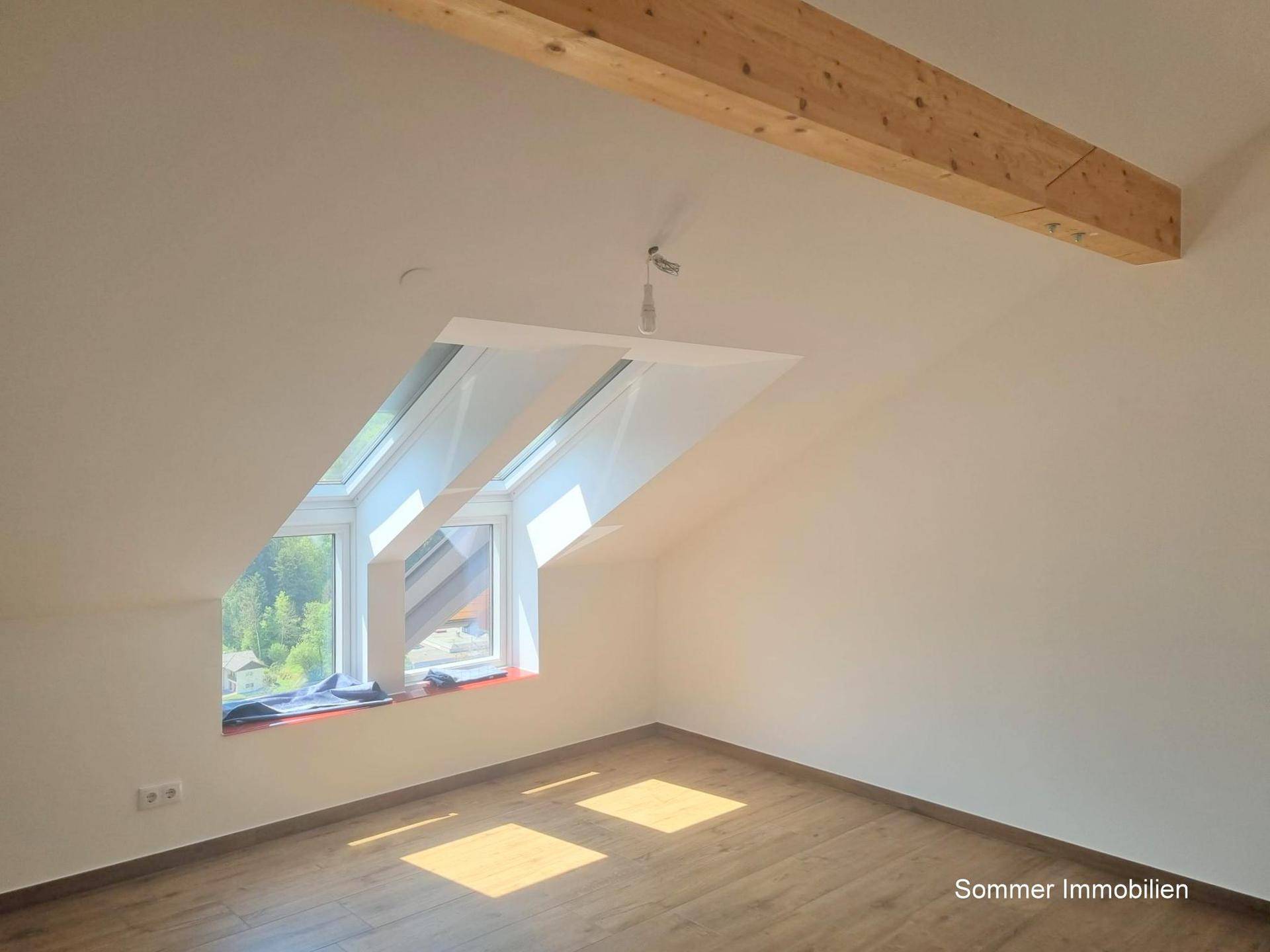 Heller Raum mit Holzboden, Dachschräge und einem großen Dachfenster für viel Tageslicht.