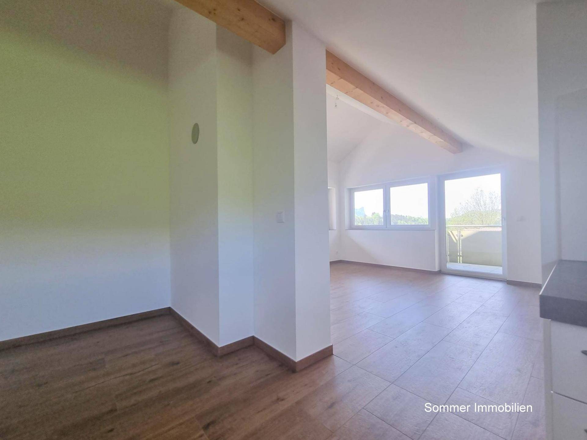 Heller Flurbereich mit Holzboden und sichtbarem Deckenbalken, der in einen Wohnraum führt.